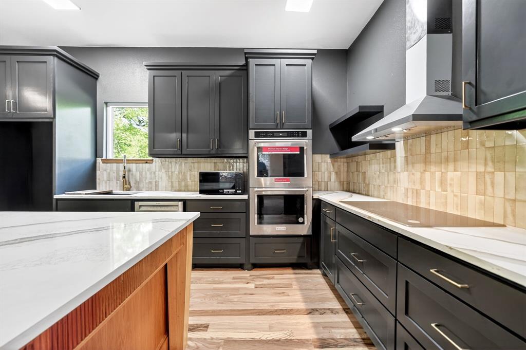 Kitchen featuring dark cabinetry, stone-finish countertops, stainless steel double wall ovens, a tile backsplash, and wood-finish flooring
