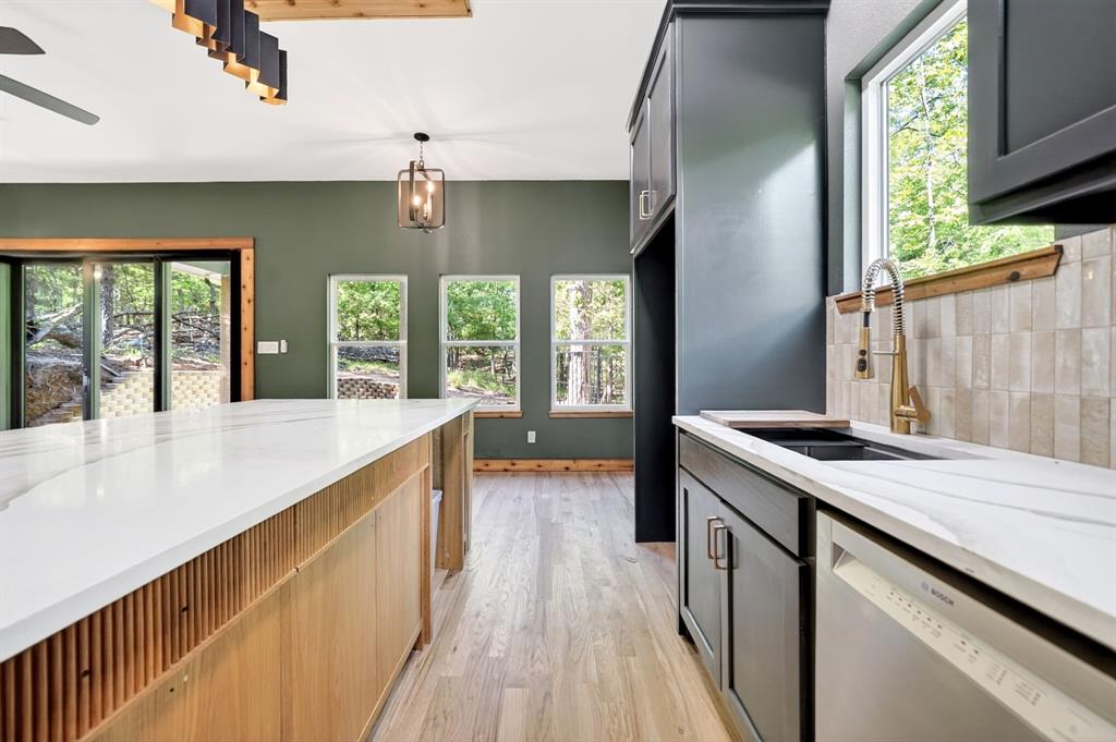 Kitchen featuring an expansive center island with fluted wood cabinetry and solid-surface countertops, custom charcoal-toned cabinetry, light-toned wood-finish flooring, textured subway tile backsplash, and metallic pull-down faucet