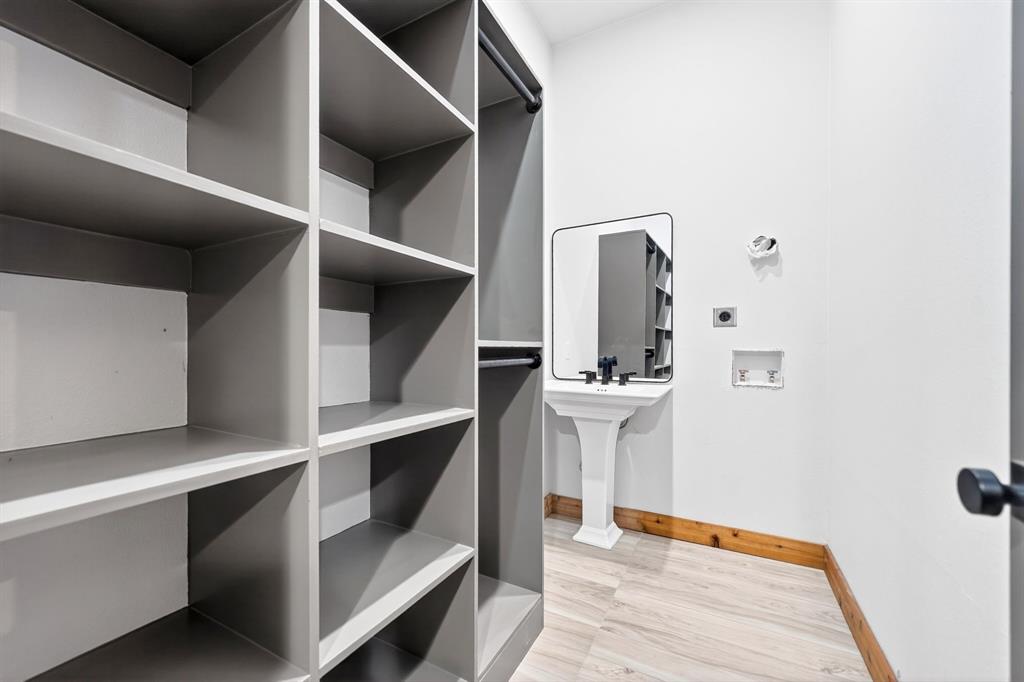 Built-in grey custom shelving, pedestal sink with matte black faucet, wall-mounted rectangular mirror, and wood-finish flooring
