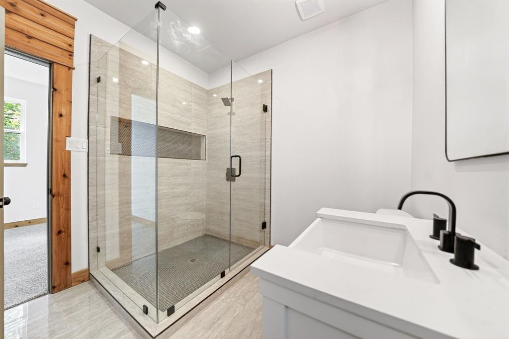 Frameless glass-enclosed shower with tiled walls and built-in niche, white vanity cabinet with stone-finish countertop, and matte black plumbing fixtures