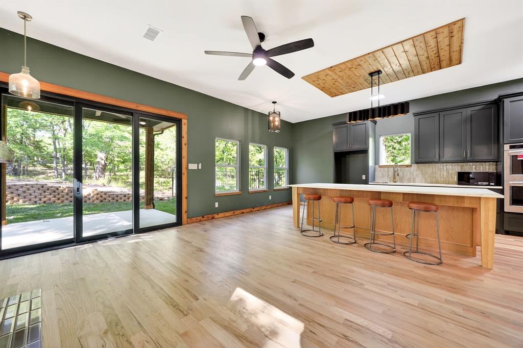 Open-concept kitchen featuring an expansive center island with seating, wood-finish flooring, custom cabinetry, a wood-paneled ceiling inlay, and sliding glass doors Open-concept kitchen featuring an expansive center island with seating, wood-finish flooring, custom cabinetry, a wood-paneled ceiling inlay, and sliding glass doors