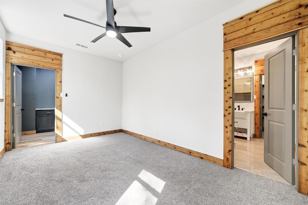 Room featuring neutral wall-to-wall carpeting, natural wood door casing, grey interior doors, and a modern matte black ceiling fan with integrated lighting