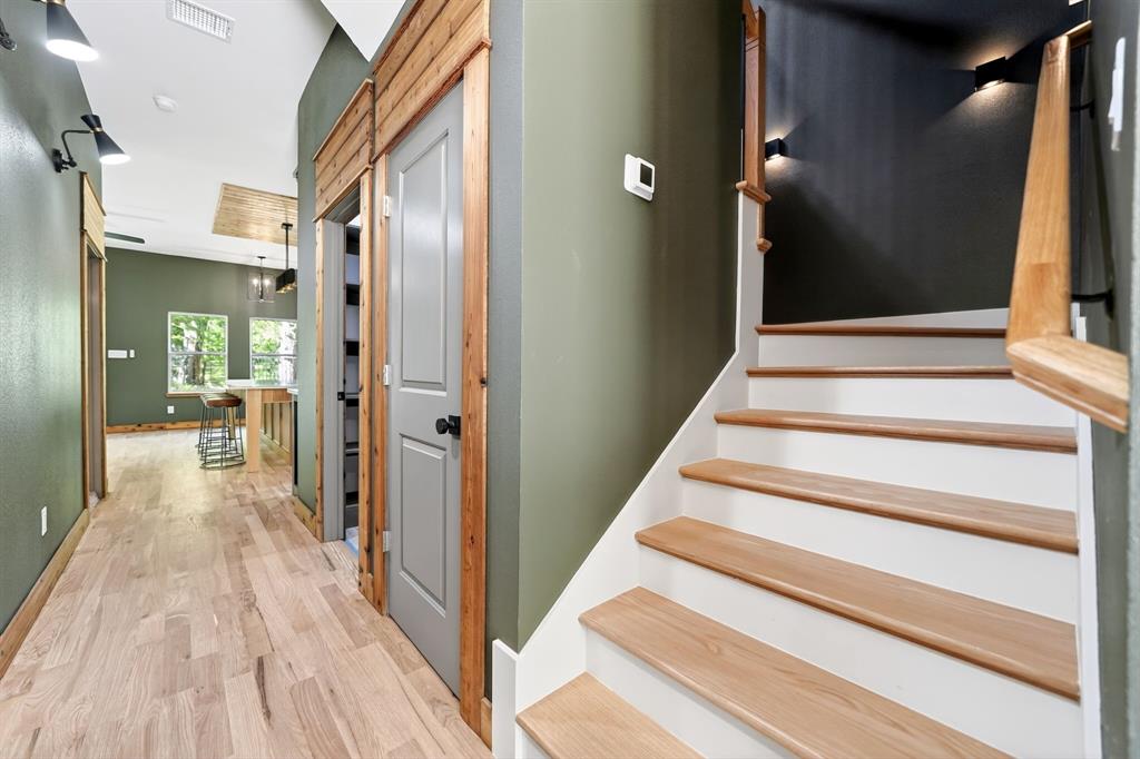 Interior staircase with natural wood treads, white risers, and a matching wood-finish handrail, complemented by natural wood door trim, wood-finish flooring, and wall-mounted task lighting