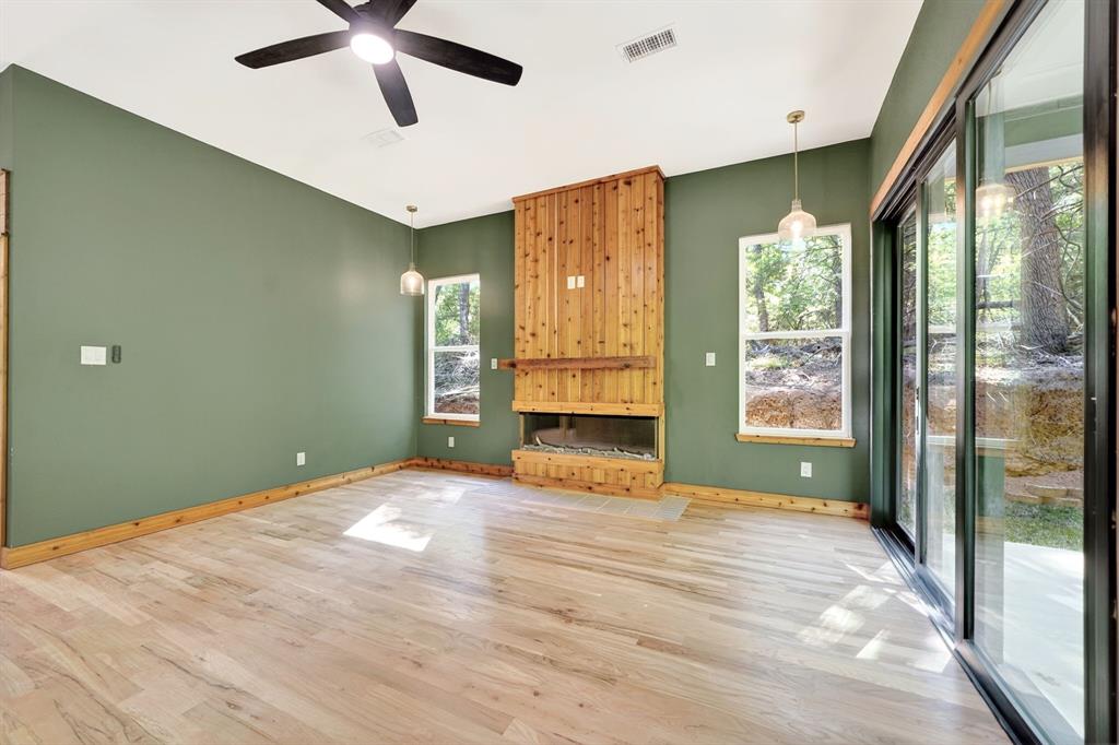Living area featuring wood-finish flooring, a floor-to-ceiling wood-clad fireplace, integrated ceiling fan, and sliding glass doors Living area featuring wood-finish flooring, a floor-to-ceiling wood-clad fireplace, integrated ceiling fan, and sliding glass doors