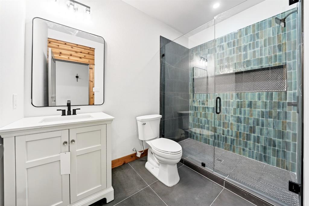 Bathroom featuring a white vanity with a rectangular sink, a frameless glass-enclosed shower with teal vertical tiling, a built-in shower niche, and dark large-format floor tile