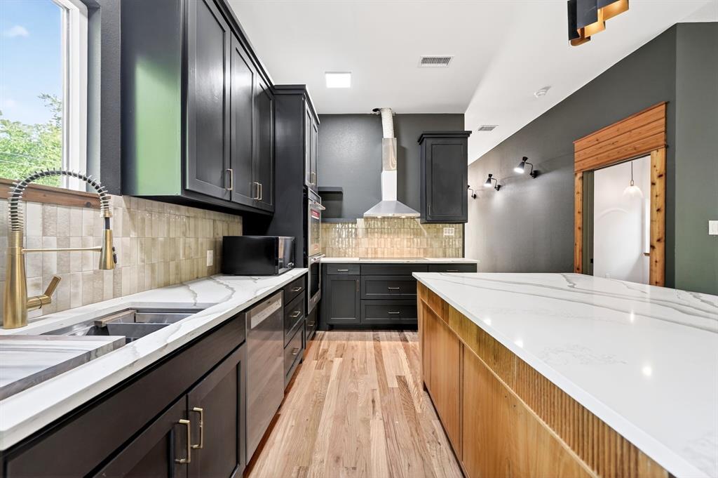 Kitchen featuring dark cabinetry, expansive stone-surface countertops, wood-finish flooring, a stainless steel range hood, and a dual-handle bridge faucet