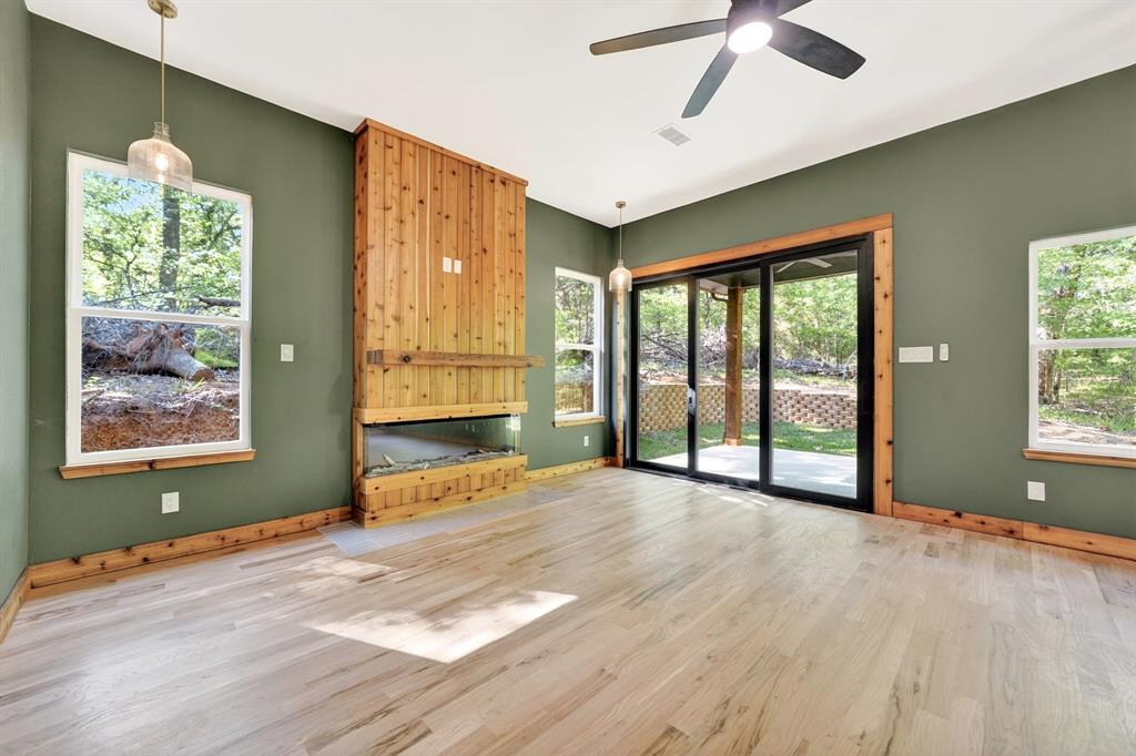 Living area featuring wood-finish flooring, a floor-to-ceiling wood-paneled fireplace, glass sliding doors, dual pendant lighting, and a ceiling fan Living area featuring wood-finish flooring, a floor-to-ceiling wood-paneled fireplace, glass sliding doors, dual pendant lighting, and a ceiling fan