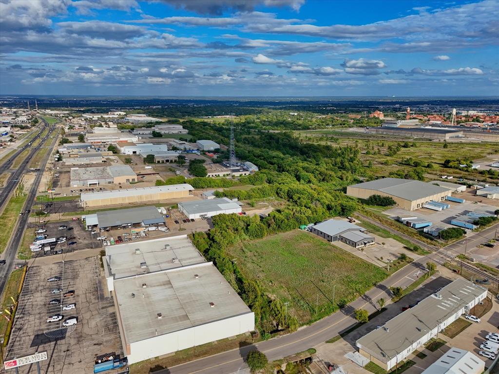Aerial perspective featuring expansive undeveloped land parcel with frontage on a paved thoroughfare, surrounded by established industrial and commercial infrastructure
