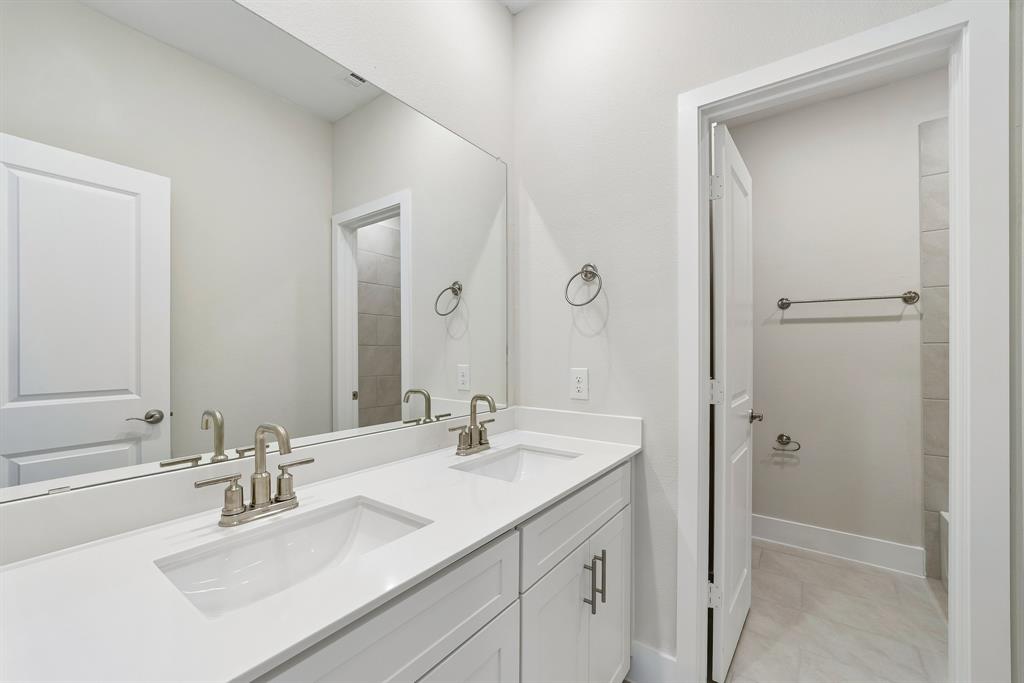 Dual-sink vanity with a solid-surface countertop, white Shaker-style cabinetry, polished metal hardware, and a large-format vanity mirror