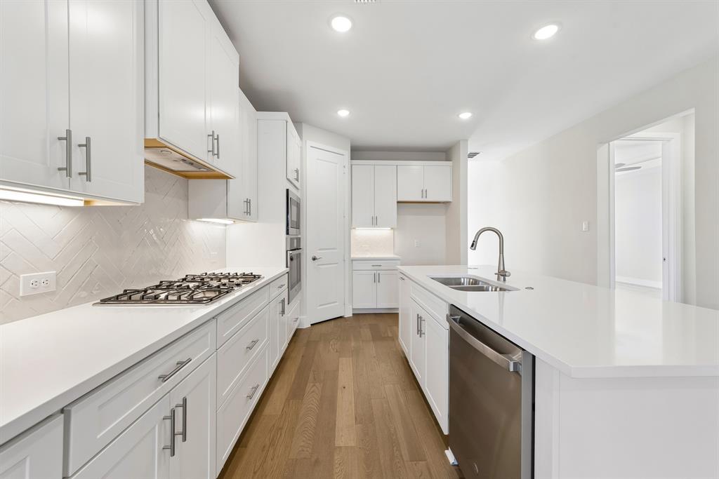 Kitchen featuring white cabinetry, quartz countertops, herringbone-patterned tile backsplash, stainless steel appliances, and wood-finish flooring