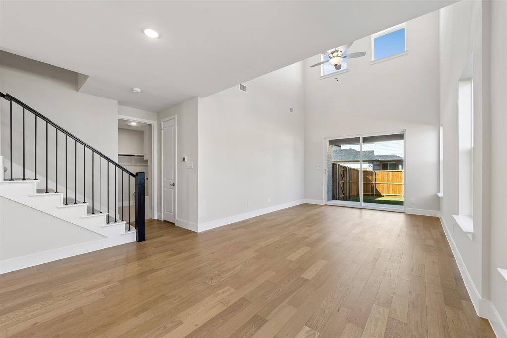 High-ceilinged interior featuring wood-finish flooring, a metal-railing staircase, recessed lighting, a ceiling fan, and sliding glass doors