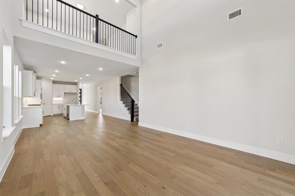 Two-story volume ceiling with a mezzanine overlook, wood-finish flooring, recessed lighting, and a kitchen featuring built-in cabinetry and a central island