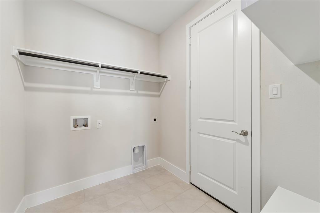 Neutral-toned utility space featuring tile flooring, a wall-mounted shelving unit, and a solid-core interior door with satin nickel hardware