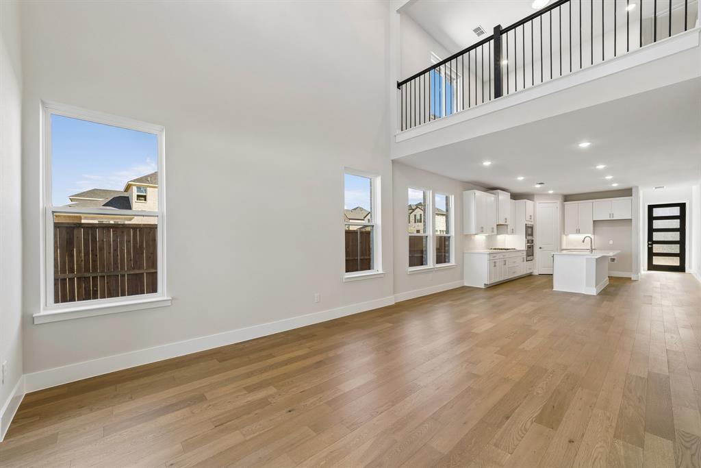 Double-height living area featuring wood-finish flooring, white shaker-style cabinetry, a central kitchen island, and an overlook with black metal balusters