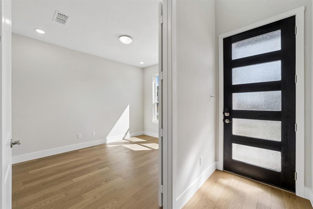 Modern entry featuring a black five-panel door with textured glass inserts, light wood-finish flooring, and recessed ceiling lighting