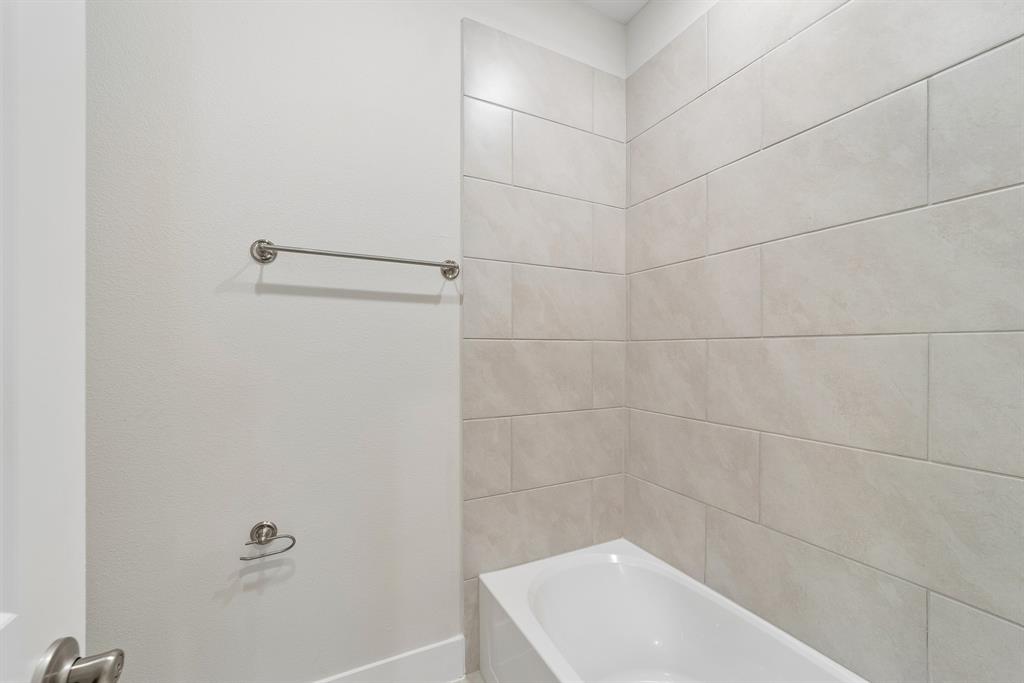 Bathtub enclosure featuring large-format ceramic wall tile, brushed nickel towel bar, and integrated toilet paper holder