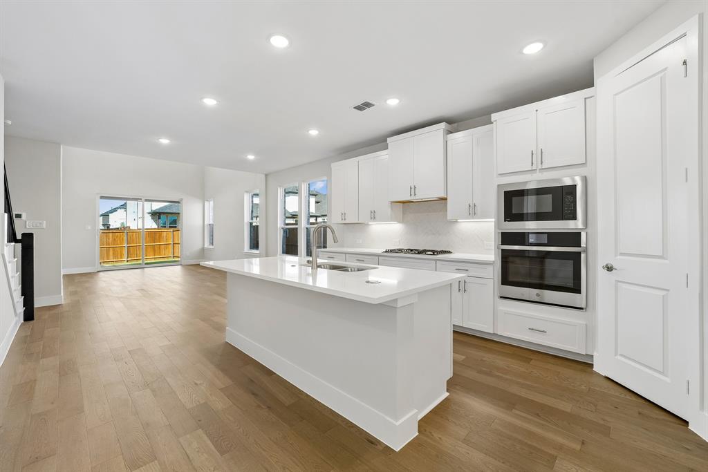 Kitchen featuring white cabinetry, quartz countertops, a central island with an undermount sink, built-in stainless steel appliances, and wood-finish flooring