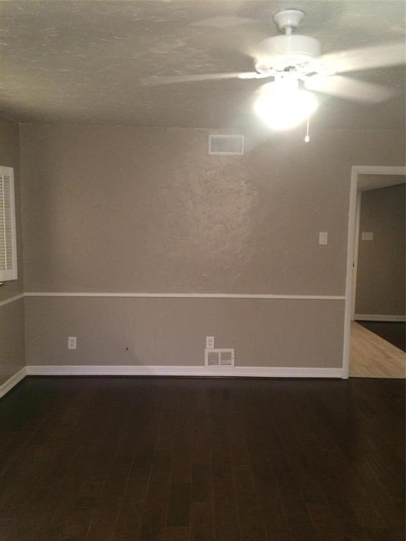 Dark-toned wood-finish flooring, textured wall surfaces, and white chair rail molding, complemented by a ceiling fan with integrated lighting and plantation-style window shutters