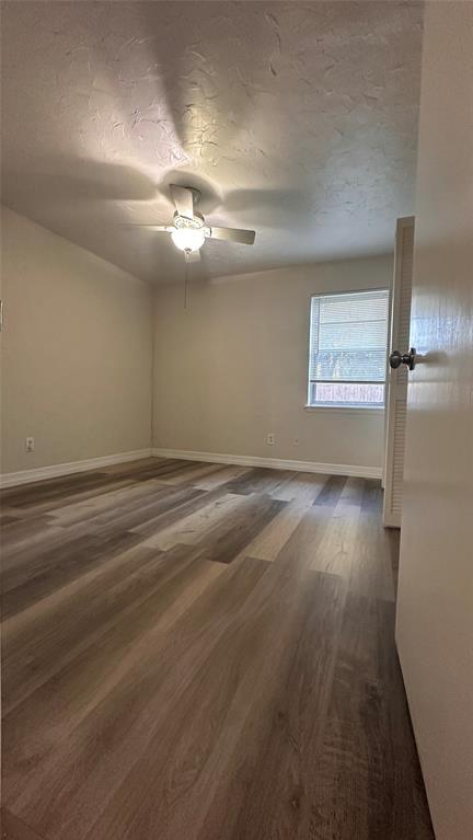 Neutral-toned room featuring multi-tonal wood-finish flooring, a ceiling fan with integrated lighting, and a single-pane window