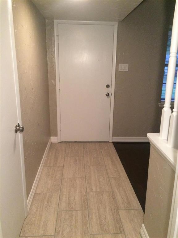 Entry area featuring light-toned rectangular floor tile, neutral textured wall finishes, a solid core white entry door with metallic hardware, and a white balustrade