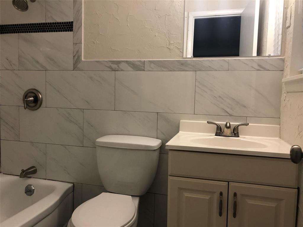 Bathroom featuring stone-finish wall tile, a built-in vanity cabinet with integrated sink, metallic double-handle faucet, and shower fixture with a decorative mosaic border