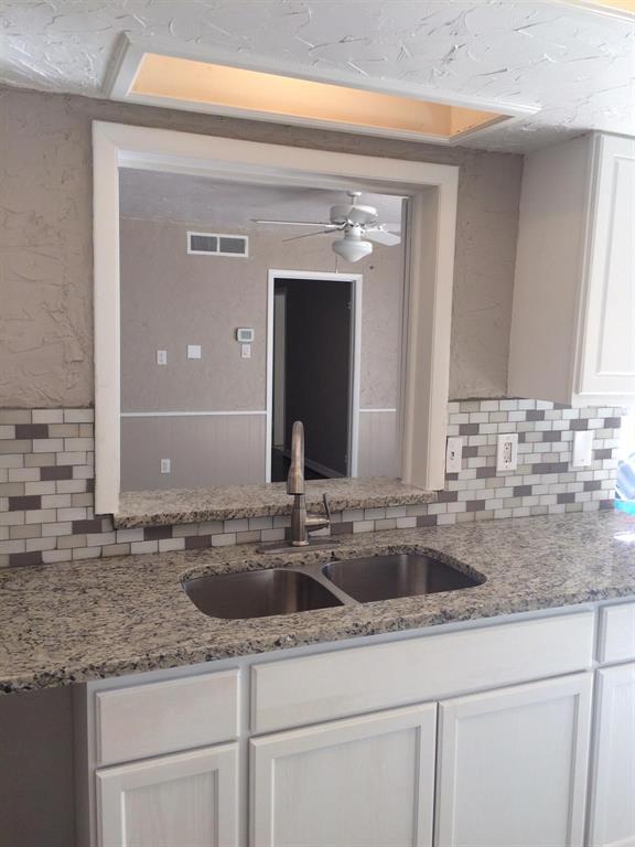 Kitchen featuring a stone-composite countertop, dual-basin stainless steel sink with a high-arch faucet, white shaker-style cabinetry, and a multi-tone mosaic tile backsplash