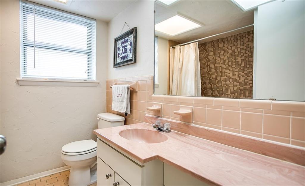 Bathroom featuring a vanity with an integrated basin, a large wall-mounted mirror, ceramic tile backsplashes, a shower with patterned tile surround, and a window with integrated blinds