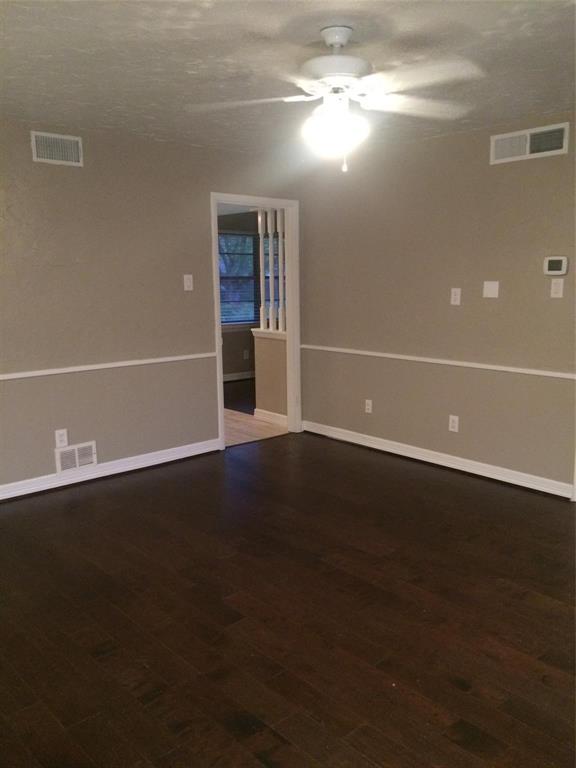 Interior space featuring dark wood-finish flooring, neutral wall tones, white chair rail molding, a ceiling fan with integrated lighting, and decorative balusters