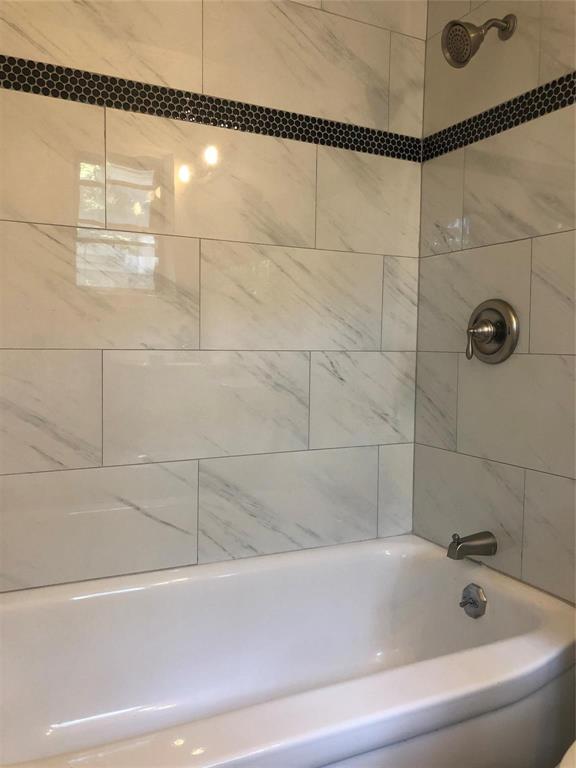 Bathtub enclosure featuring large-format stone-patterned wall tile, a decorative circular mosaic accent border, and brushed metal fixtures
