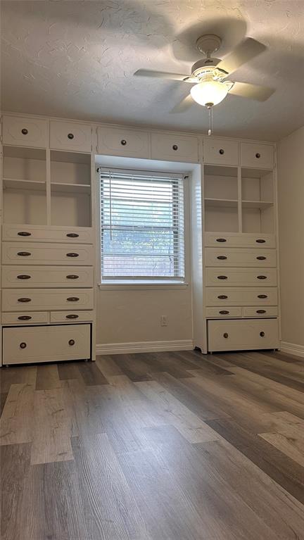 Built-in floor-to-ceiling cabinetry with overhead storage, wood-finish flooring, and a central ceiling fan with integrated lighting