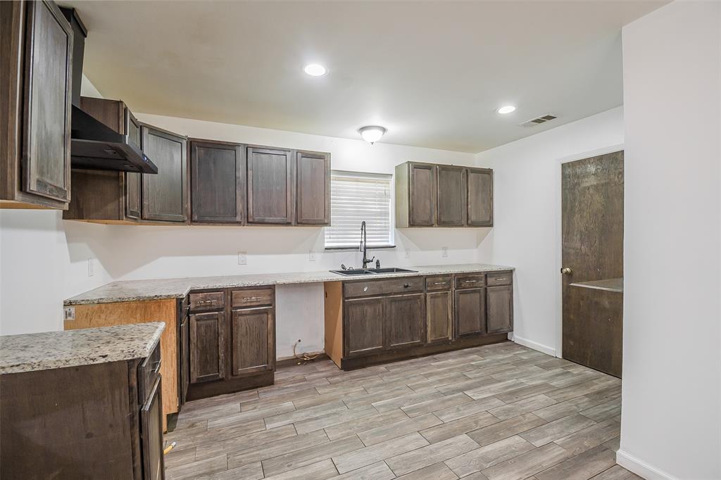 Kitchen featuring dark-toned cabinetry, stone-finish countertops, wood-finish flooring, recessed lighting, and a gooseneck faucet