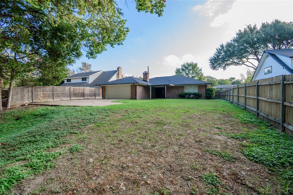 Expansive backyard featuring a concrete patio, brick exterior, attached garage, and wood privacy fencing