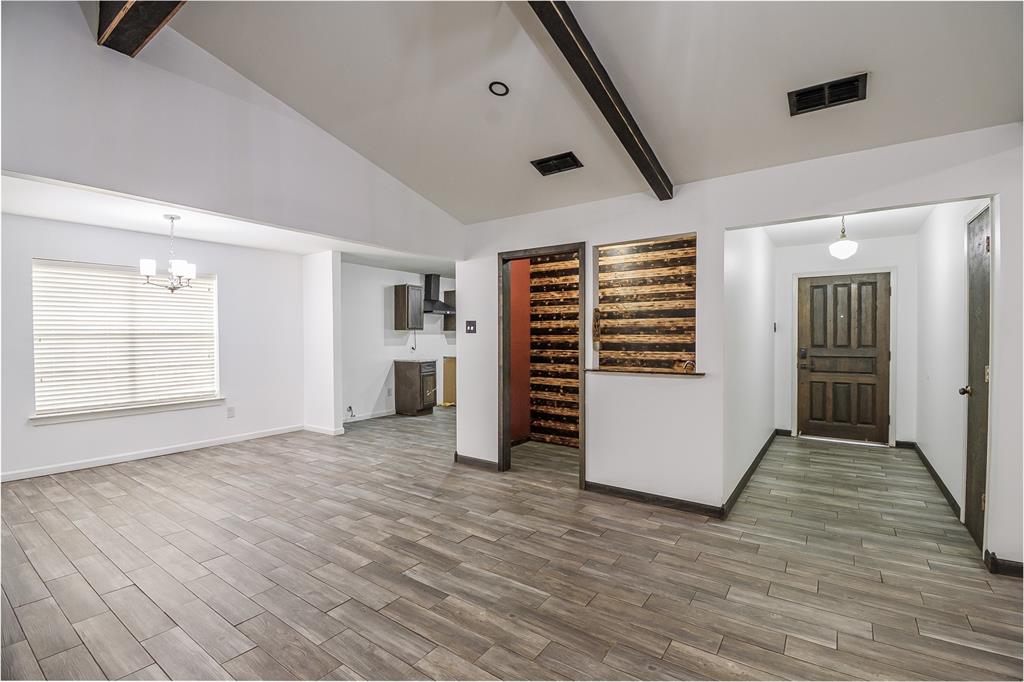 Vaulted ceilings with exposed structural beams, wood-finish tile flooring, a multi-paneled wood entry door, and a decorative horizontal-slat wall feature Vaulted ceilings with exposed structural beams, wood-finish tile flooring, a multi-paneled wood entry door, and a decorative horizontal-slat wall feature