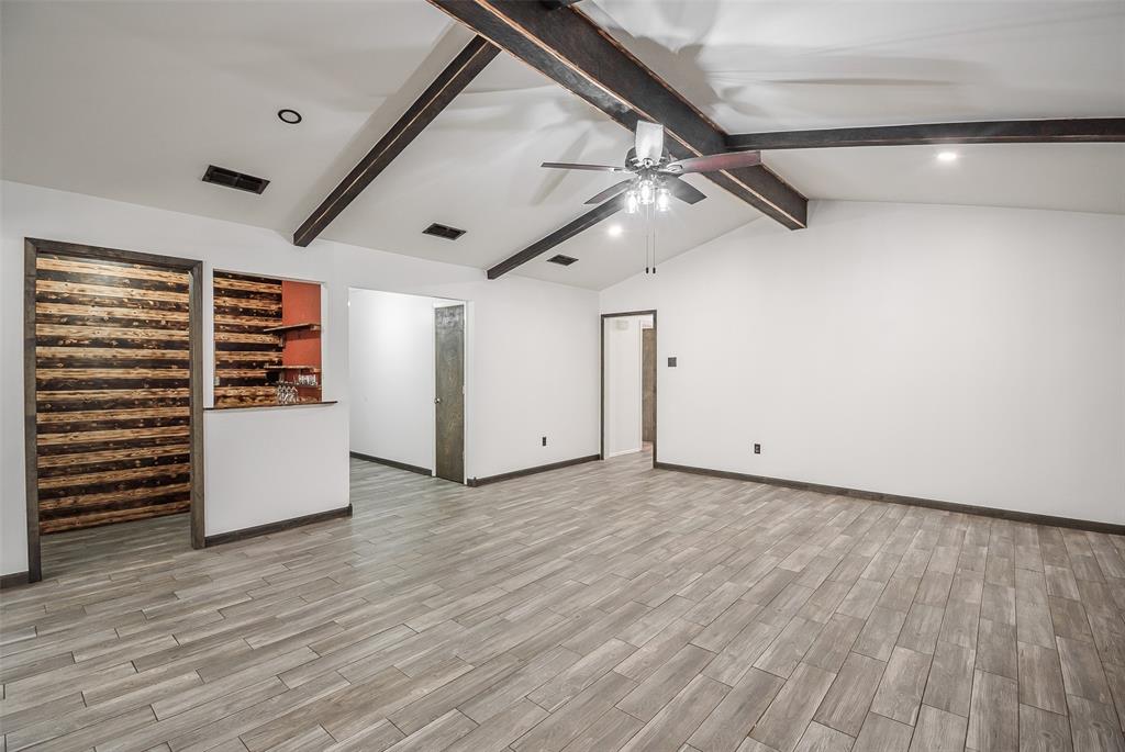 Vaulted ceiling with exposed wood beams, wood-finish tile flooring, recessed lighting, and a built-in architectural accent wall