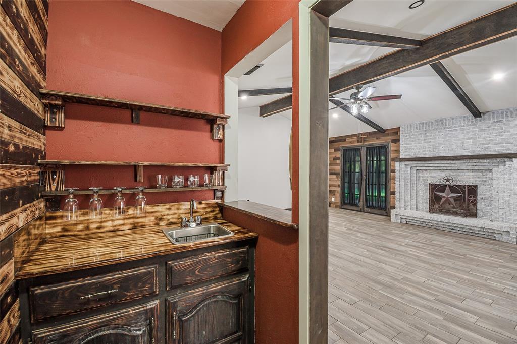 Built-in wet bar featuring custom wood cabinetry, wood-finish countertops, floating shelving, and an inset stainless steel sink