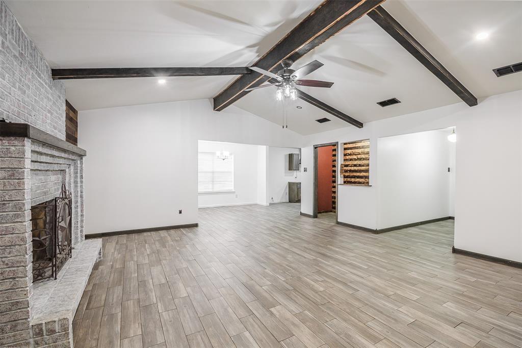 Vaulted ceiling with exposed wood beams, brick fireplace featuring a raised hearth, and wood-finish flooring