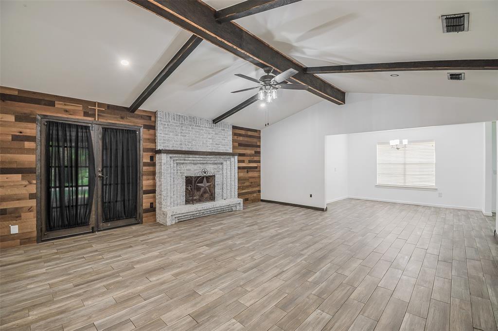 Living area featuring a vaulted ceiling with exposed beams, wood-finish flooring, a white-washed brick fireplace, and an accent wall with natural wood planks Living area featuring a vaulted ceiling with exposed beams, wood-finish flooring, a white-washed brick fireplace, and an accent wall with natural wood planks