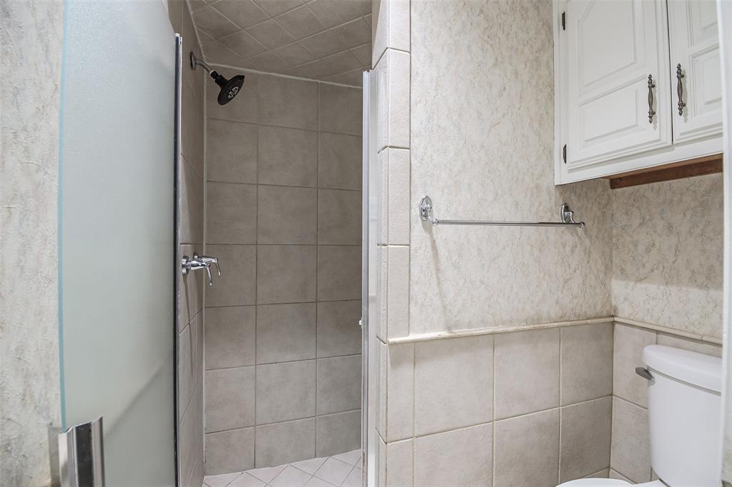 Shower enclosure featuring large-format ceramic tile, frosted glass door, and a wall-mounted showerhead, complemented by built-in white cabinetry and a dual-handle faucet