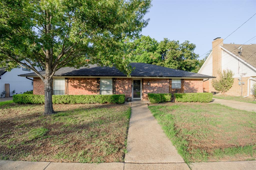 Single-story brick exterior featuring a multi-gable roofline, mature trees, and a concrete walkway Single-story brick exterior featuring a multi-gable roofline, mature trees, and a concrete walkway