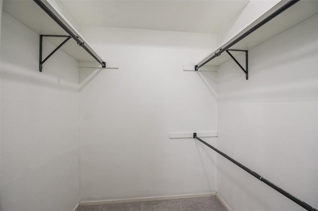 Storage closet featuring dual-level white shelving and matte black metal hanging rods