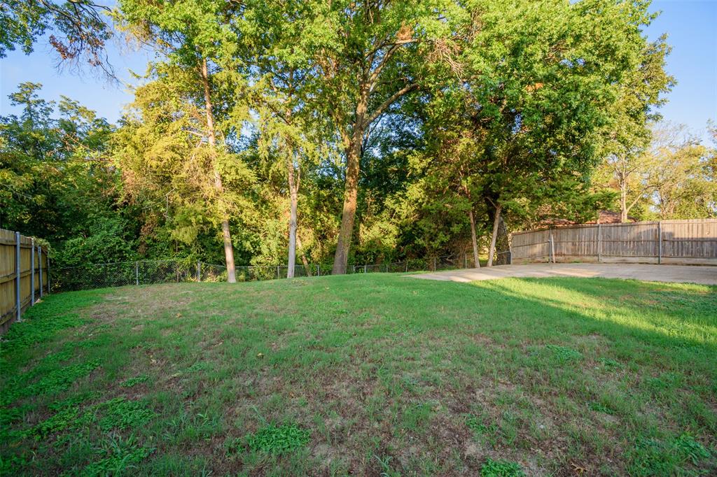Backyard featuring a grass lawn, concrete patio, wooden perimeter fencing, and mature trees