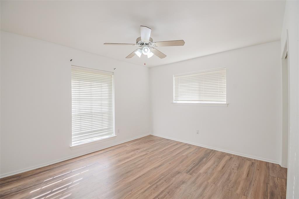 Neutral-toned interior featuring wood-finish flooring, two windows with installed blinds, and a central ceiling fan with integrated lighting