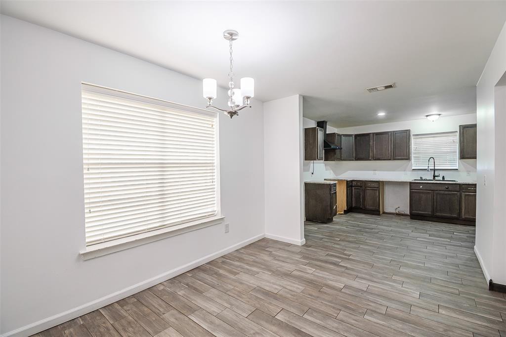 Open-concept interior featuring wood-finish flooring, dark-toned cabinetry, a multi-light chandelier, and large windows with integrated blinds