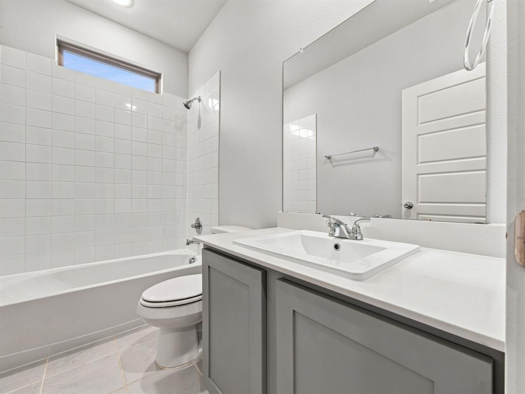Bathroom featuring a grey vanity with a solid surface countertop, undermount sink, full-width mirror, and a tub-shower combination with floor-to-ceiling tile surround and transom window