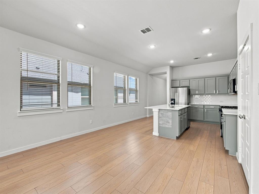 Open-concept interior featuring wood-finish flooring, recessed lighting, a center island with a stone-surface countertop, and grey shaker-style cabinetry with tile backsplash