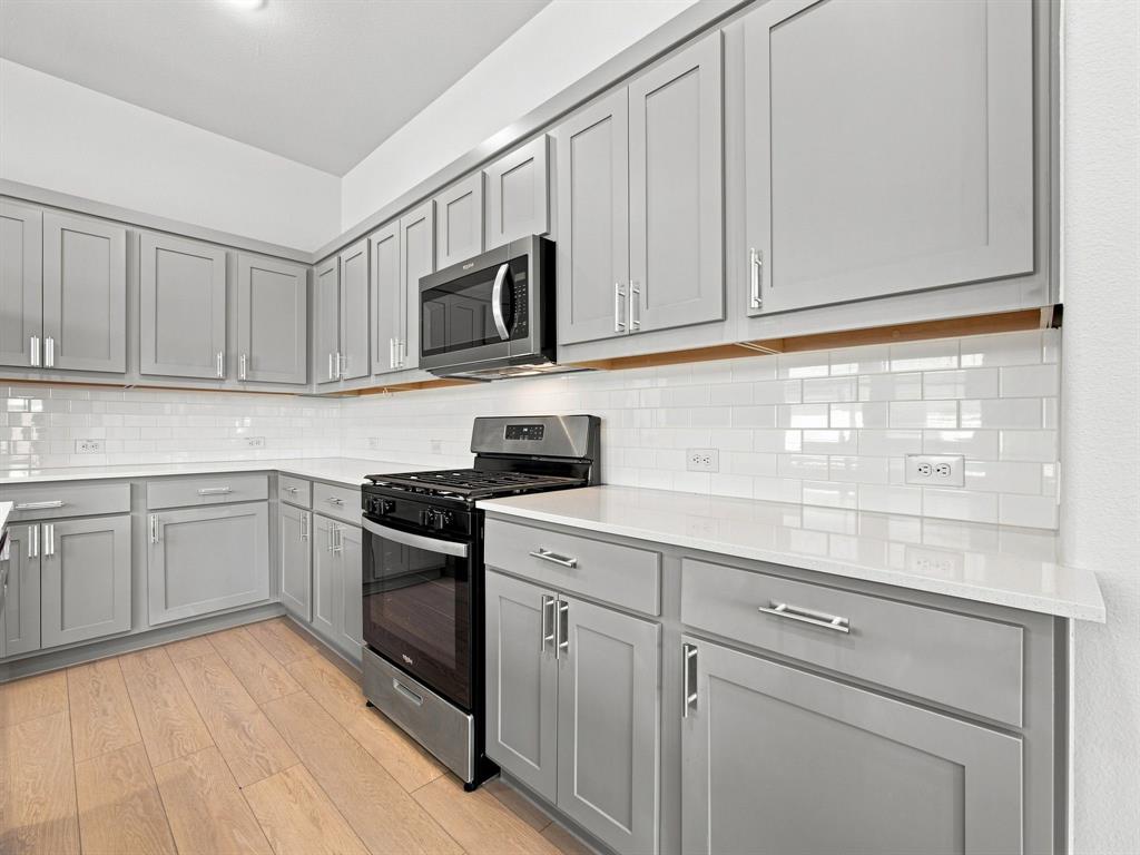 Kitchen featuring shaker-style grey cabinetry, white solid-surface countertops, white subway tile backsplash, wood-finish flooring, and stainless steel appliances