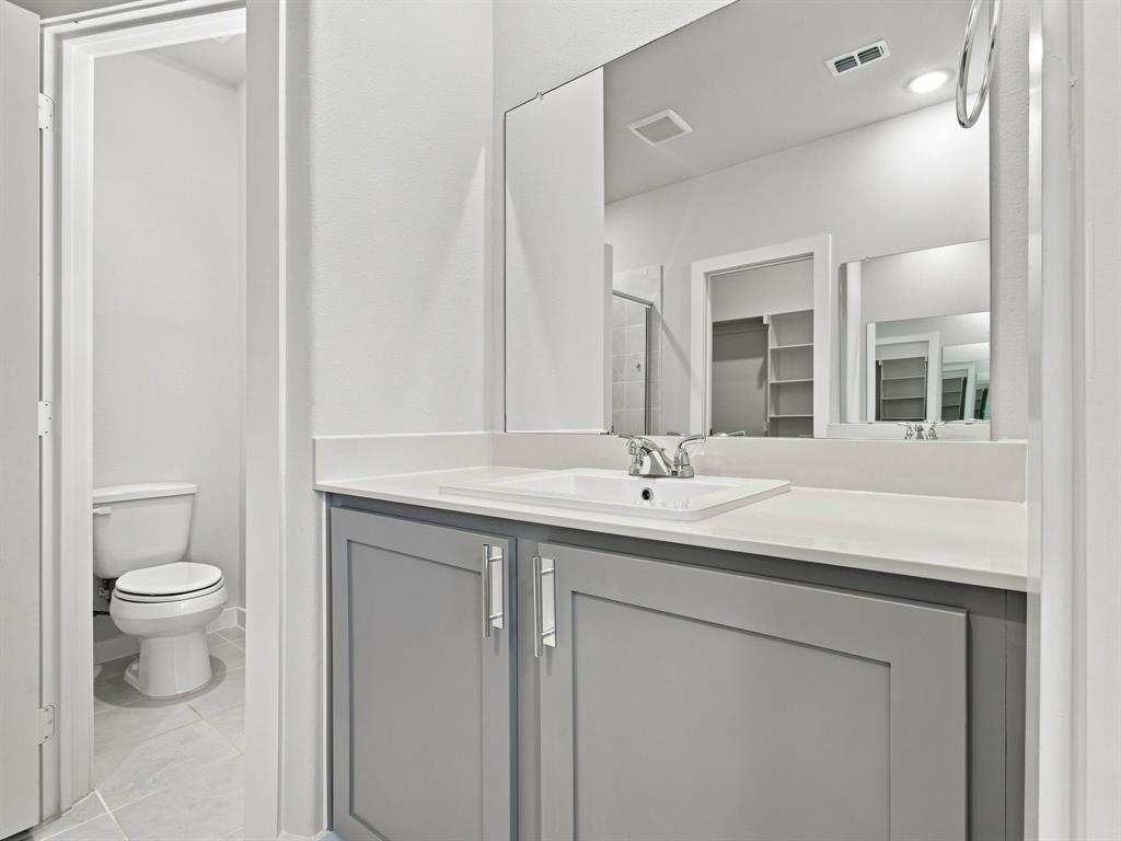 Bathroom vanity featuring a grey shaker-style cabinet, white solid-surface countertop, integrated rectangular sink, polished chrome faucet, and expansive wall-mounted mirror