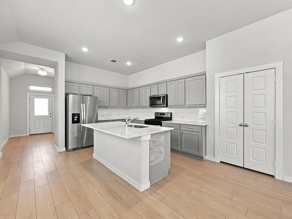 Kitchen featuring a central island with a solid surface countertop, light-toned wood-finish flooring, shaker-style cabinetry, recessed lighting, and stainless steel appliances