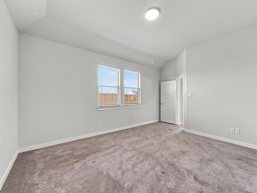 Neutral-toned room featuring a vaulted ceiling, plush wall-to-wall carpeting, two double-hung windows with horizontal blinds, and a paneled interior door