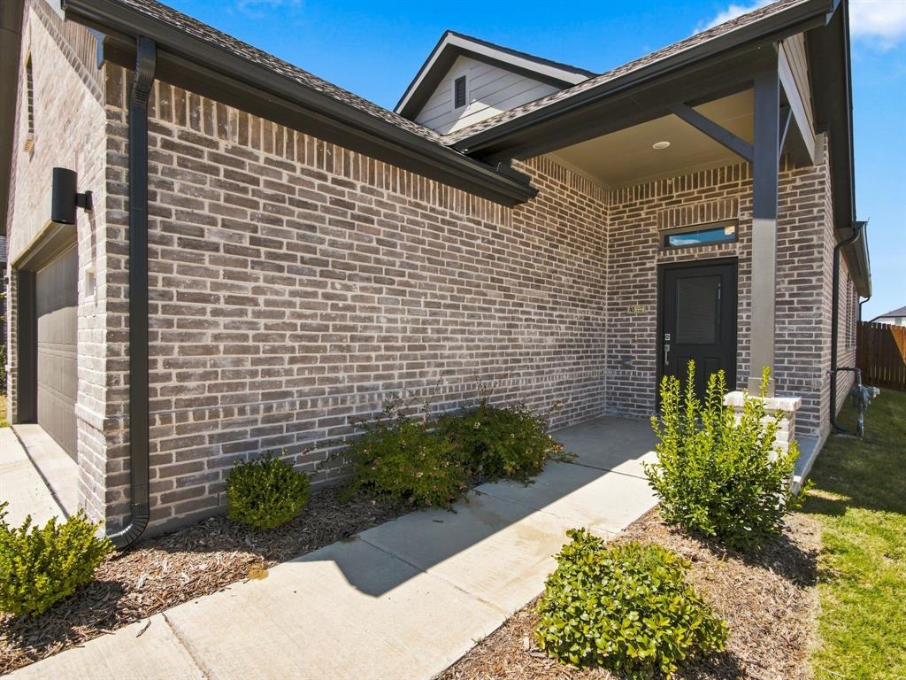 Brick exterior featuring a covered front porch, dark-toned trim, concrete walkway, and recessed entry lighting